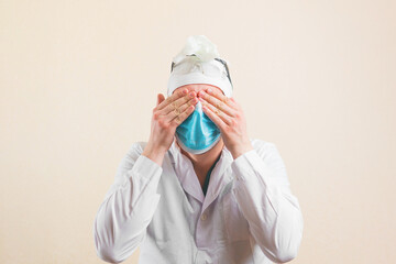 Shocked doctor with hands on his eyes in protective medical mask and white lab coat isolated