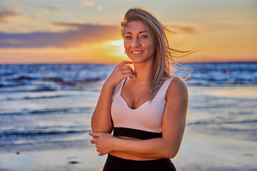 Fototapeta na wymiar Smiling woman is standing on coast during sunset.
