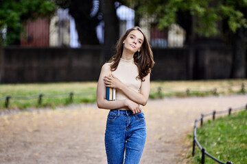 Fototapeta premium Slim female student holds books in public park.