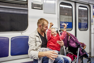 Cheerful toddler girl play while sitting in subway train with father.