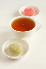 Two types of Japanese dessert mochi - pomegranate with honey and green matcha tea on a small white bowls and a cup of green tea on a white wooden table. Closeup