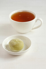 Green matcha tea Japanese dessert mochi on a white saucer and a cup of green tea on a white wooden table. Closeup