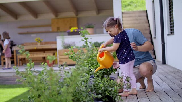 Father with small daughters outdoors in tha backyard, watering plants.