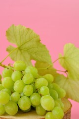 Grape. A bunch of green grapes with leaves on a light pink background.Organic natural fruits 