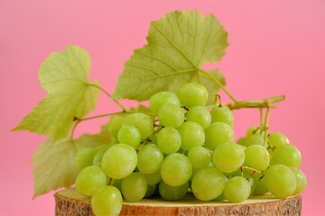 Grape. A bunch of green grapes with leaves on a light pink background.Organic natural fruits and berries
