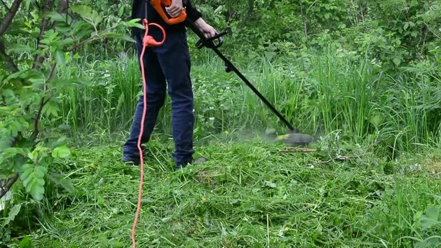 A man mows the grass with an electric trimer in the garden. Mowing grass.
