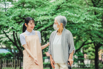 高齢者をサポートするエプロン姿の女性（杖）
