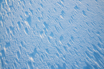 Beautiful winter background with snowy ground. Natural snow texture. Wind sculpted patterns on snow surface.
