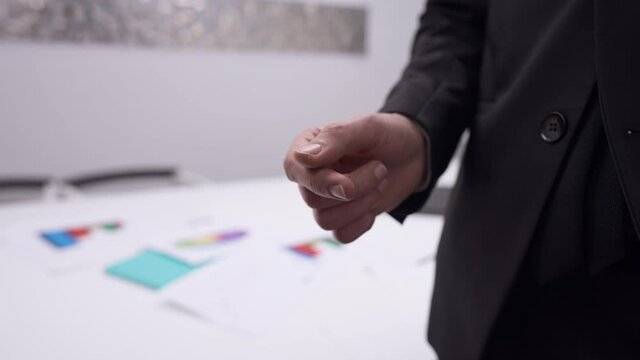 Close-up male Caucasian hands passing business card in slow motion and shaking. Unrecognizable partners making deal exchanging contacts indoors in office. Entrepreneurship and cooperation