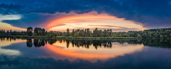 Wonderful summer morning over the lake. The colored sky is reflected in the water.