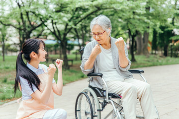 車椅子に乗った高齢者女性と女性スタッフ（ガッツポーズ）
