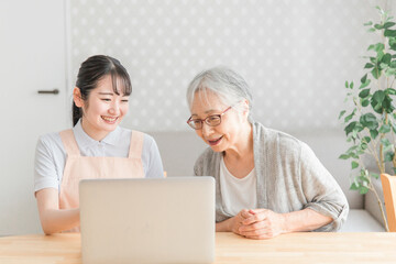 パソコンを使うエプロン姿の女性と高齢者（教える）
