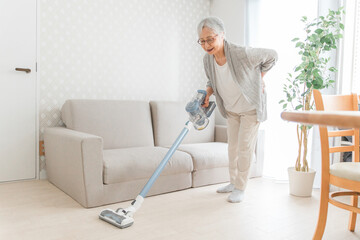 部屋を掃除する高齢者女性（腰痛）
 - obrazy, fototapety, plakaty