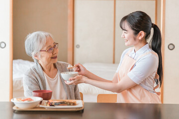 食事をする高齢者女性と女性スタッフ（食事介助）
