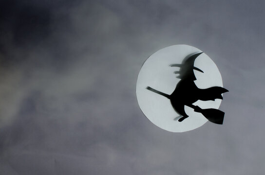 The shadow of a black witch flying on a broomstick in the clouds of fog against the background of the moon. A mock-up of an invitation for Halloween.