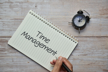 Holding a pen with TIME MANAGEMENT on notebook and analog alarm clock. Business concept.