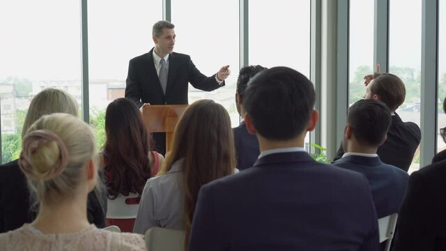 senior businessman standing at podium giving a speech addressing a conference in  seminar. old executive man presentation in Meeting at office  with colleagues raising hand up to question from speaker