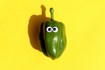 Abstract illustration. Green pepper with glued eyes lies on a yellow background.