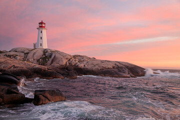 Peggy’s Cove Lighthouse illuminated at sunset with dramatic waves on the foreground, Nova Scotia,...