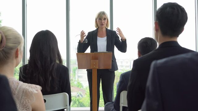 senior businesswoman standing at podium giving a speech addressing a conference in  seminar. old executive women presentation in Meeting at office on window with colleagues