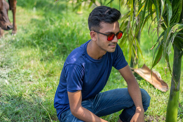 A young boy is sitting on the ground wearing a dark blue shirt and black sunglasses with styling and his behind the background blur.