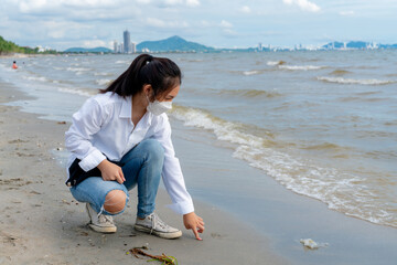 A young Asian woman in a white shirt is sitting on the beach with soft waves on a clear day.