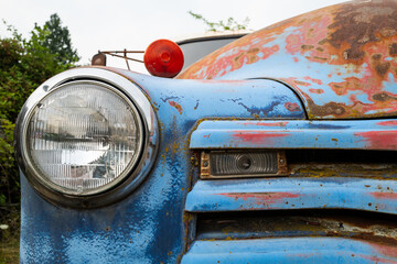 Headlight and grille on a rusty blue antique truck