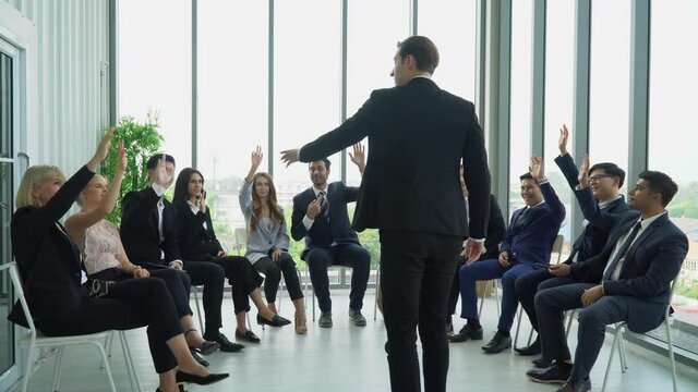 Rear back view of businessman standing giving a speech addressing a conference in  seminar. executive man presentation in Meeting at office  with colleagues raising hand up to question from speaker