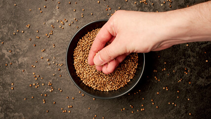 TOP VIEW: Human hand takes a pinch from a dish with coriander seeds - 457637910