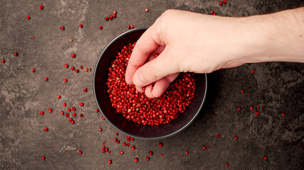 TOP VIEW: Human hand takes a pinch from a dish with pink pepper seeds - 457637924