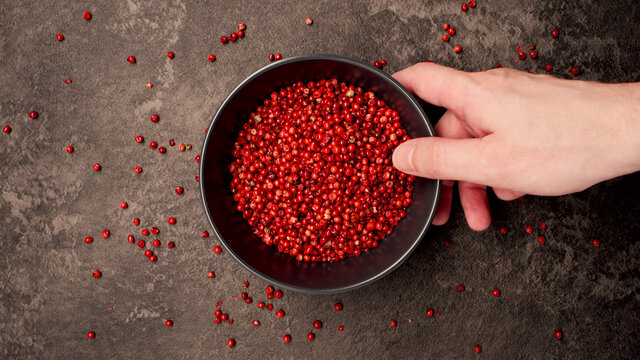 TOP VIEW: Human hand takes a dish with pink pepper seeds from a table