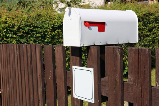 White metal mailbox mounted on a rustic fence