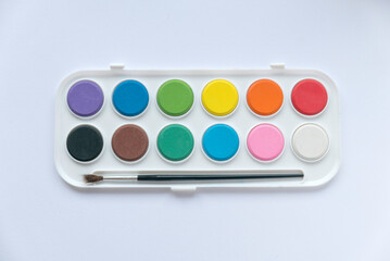 Top view of colorful watercolor palette with brush on white background.