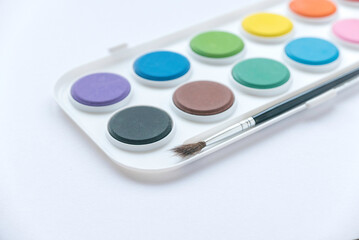 Selective focus of colorful watercolor palette with brush on white background.