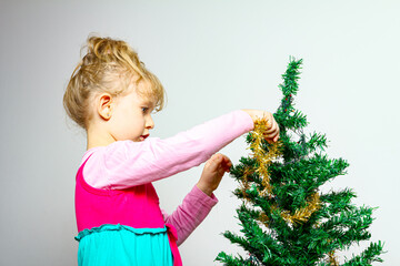 Child girl is arranging ornament decoration on artificial Christmas tree