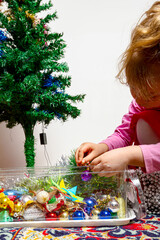 Child girl is arranging ornament decoration on artificial Christmas tree
