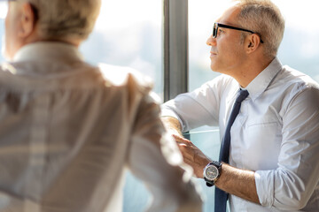 Obraz premium Picture of young business man taking to his older business partner. They are in white shirt and black tie. They are in a hotel lobby. 