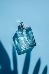 Transparent bottle of perfume on a blue background. Fragrance presentation with daylight. Trending...