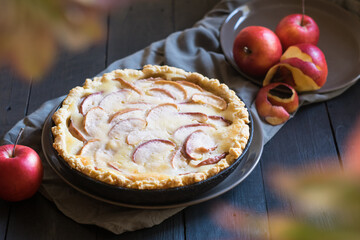 Whole apple cream pie with ripe red apples on black table, selective focus