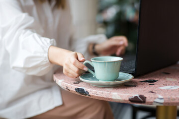 cup of coffee and laptop close-up on table in cafe. hand of business woman with nude manicure takes mug. freelance work