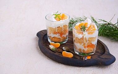 Layered dessert in a glass of shortbread, fresh mandarin and whipped cream in the Christmas and New Year's style on a brown wooden board on a light background concrete. Desserts in a glass.