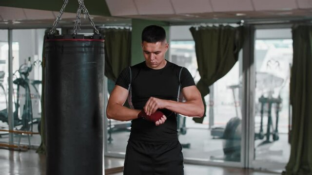 Young man boxer binds his hand with red bandages and looking in the camera