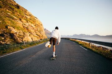 Millennial hipster man push to gain speed on skateboard. Man on longboard ride into sunset. Summer...
