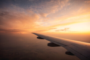 Fototapeta na wymiar Flying high over endless fields Airplane wing and sunset. Long flight abroad. Tourism and travel.