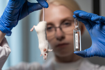 The scientist holds a white mouse by the tail in front of his face. And also the laboratory assistant holds a glass ampoule with a special preparation. Science and medicine. Close-up, blurred
