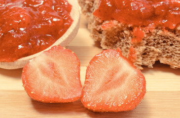 Fruits, strawberry jam on wooden spoon and wheat or rye bread in background