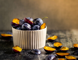 ripe blue plums in a ceramic plate on a bright background