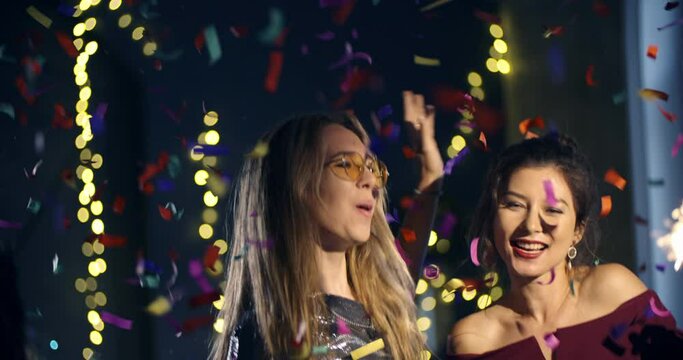 4k ProRes 422. Two young women celebrates dance the new year, Christmas, holiday, birthday. Blow up a and flies around confetti,friendship, corporate.