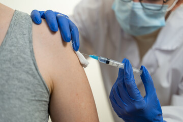 The doctor vaccinates the patient in the shoulder. Syringe, bandage, antiseptic. A typical day at the hospital. Close-up, blurred background.