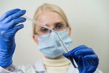 Woman scientist with a glass flask and a pipette in her hands. A laboratory assistant drips a clear liquid into a flask with a special preparation. Scientific experiment. Close-up, blurred background.